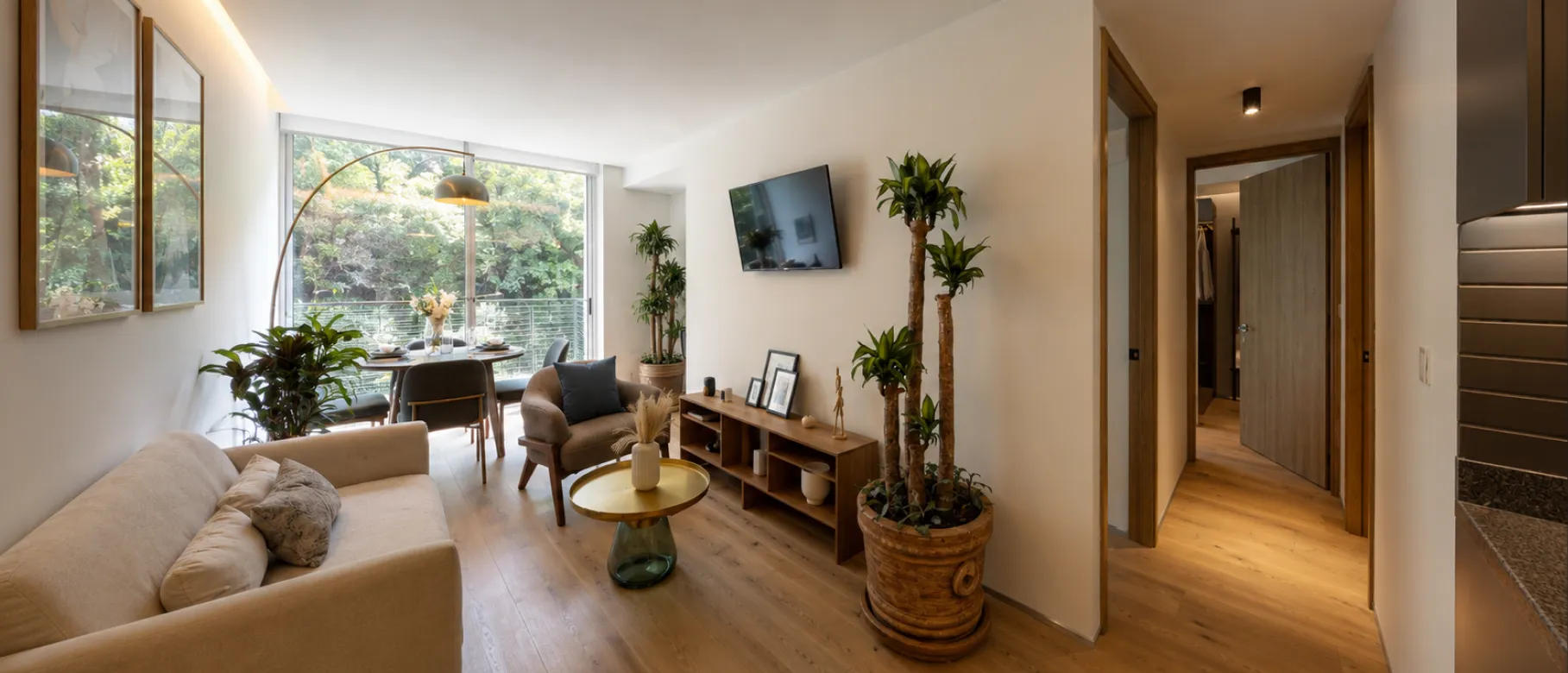 Estancia con sofá, televisión y comedor junto al ventanal en un departamento de Alure Insurgentes
